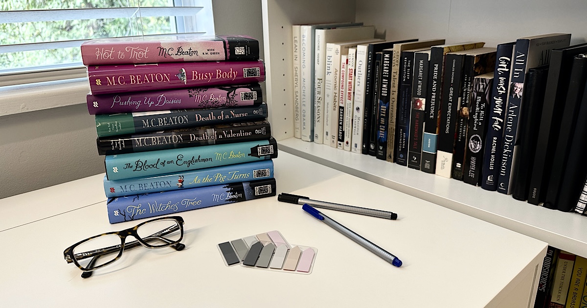 A pile of books by M.C. Beaton on a desk