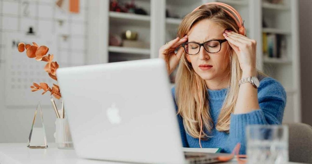 woman-sitting-in-front-of-computer-with hands-on-temples