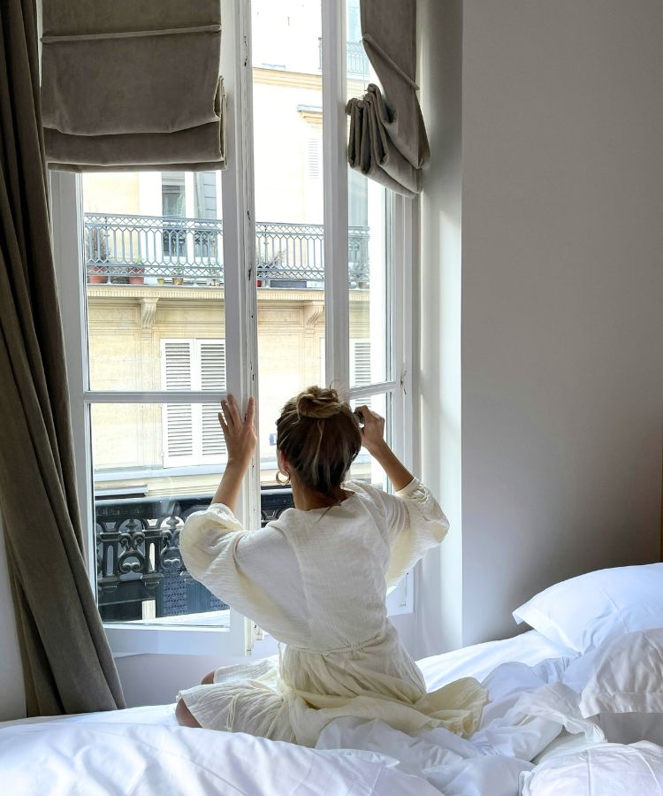 Woman sitting on bed opening the shutters