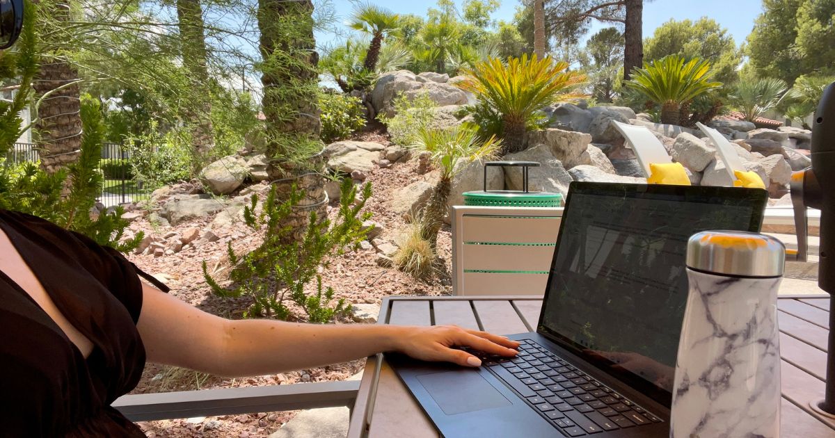 A woman studying on a laptop in the summer outside with palm trees in the background.