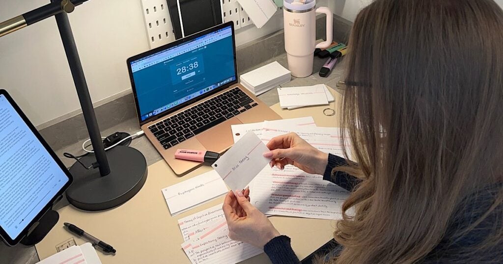 A female student studying flashcards at a desk with an open laptop showing a pomodoro timer.