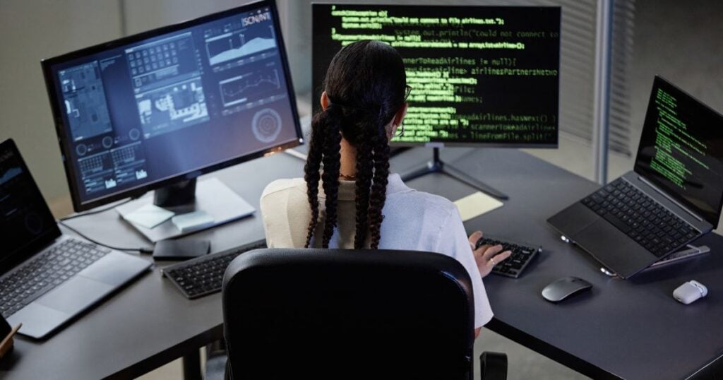 A woman at a desk in front of three computer screens doing computer coding