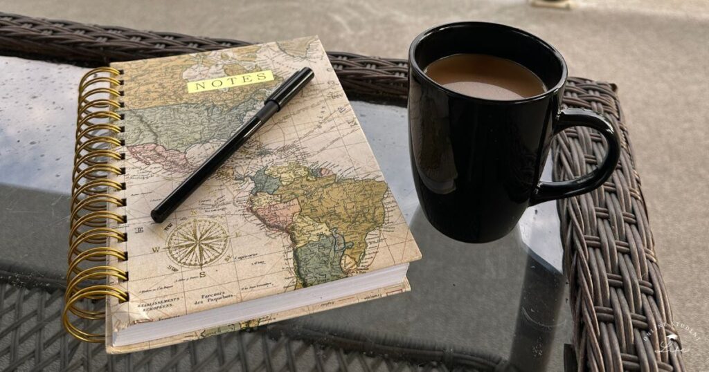 Coffee cup and travel journal on an outdoor patio table.